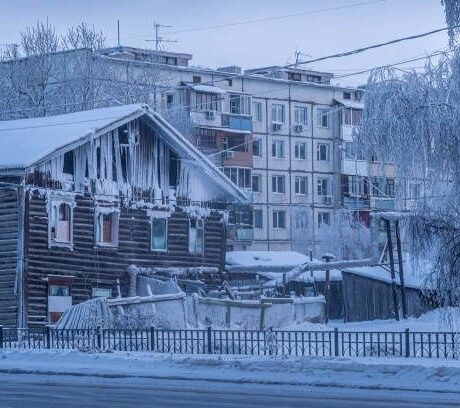Snow-covered wooden house and apartment blocks in winter Yakutsk