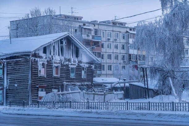 Snow-covered wooden house and apartment blocks in winter Yakutsk